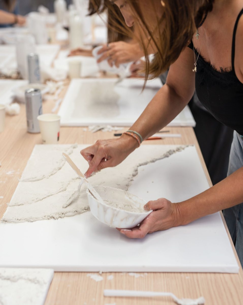 Manos aplicando pasta con textura sobre un lienzo blanco