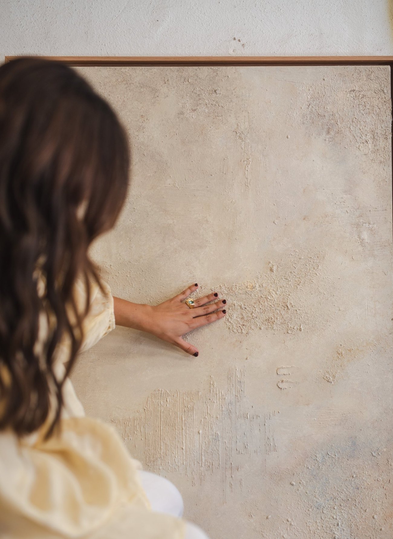 Detalle de la mano de Irene sobre la textura de un cuadro de la serie Origen, en tonos neutros