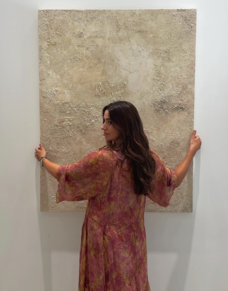 Irene sujetando un cuadro de texturas en tonos neutros, de la exposición Entre Capas