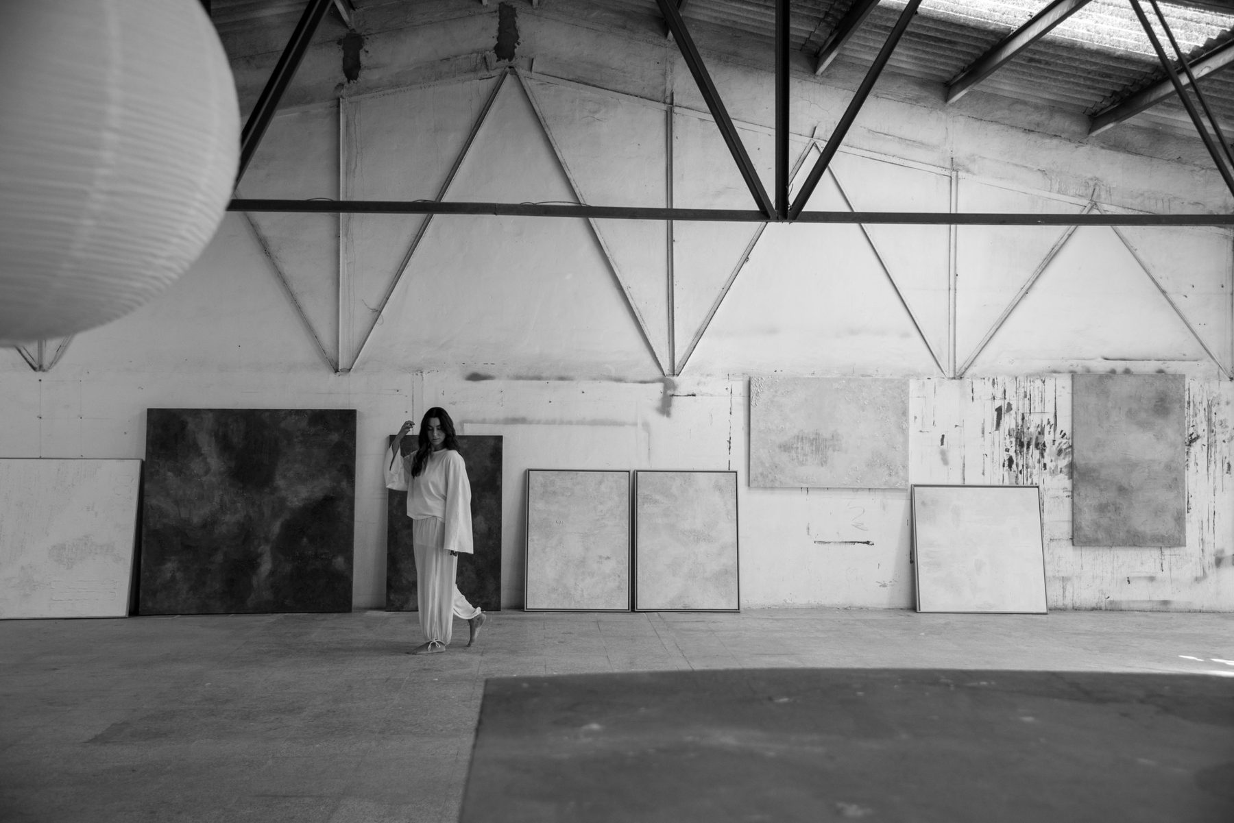 Irene caminando por la nave del estudio, entre lienzos apoyados en la pared, en blanco y negro